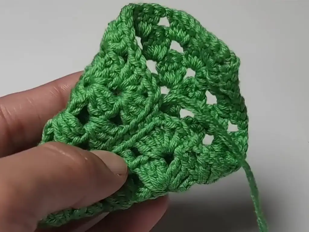 Folding a crocheted granny square diagonally to form a Christmas tree shape.