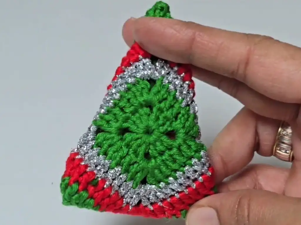Hand holding the completed crochet Christmas tree motif before seaming and adding the trunk.