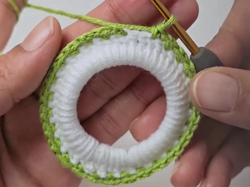 Close-up of hands crocheting, changing the color of the yarn to green.