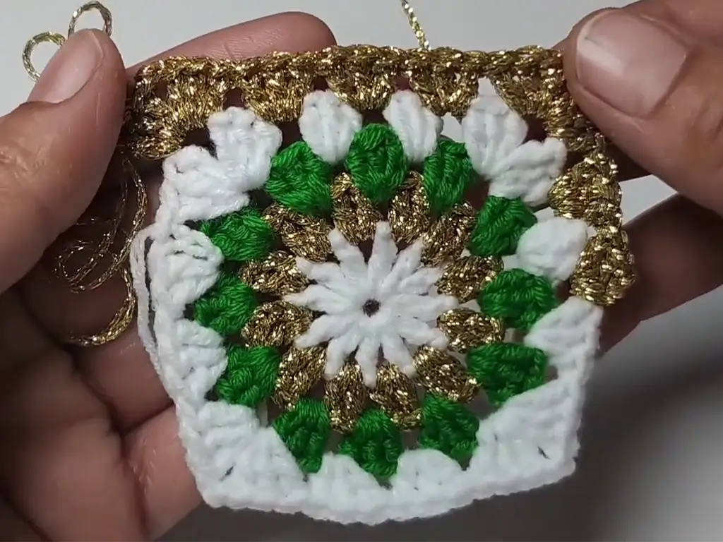 Hands holding the folded crochet Christmas tree granny square, ready for sewing to create the cone shape.