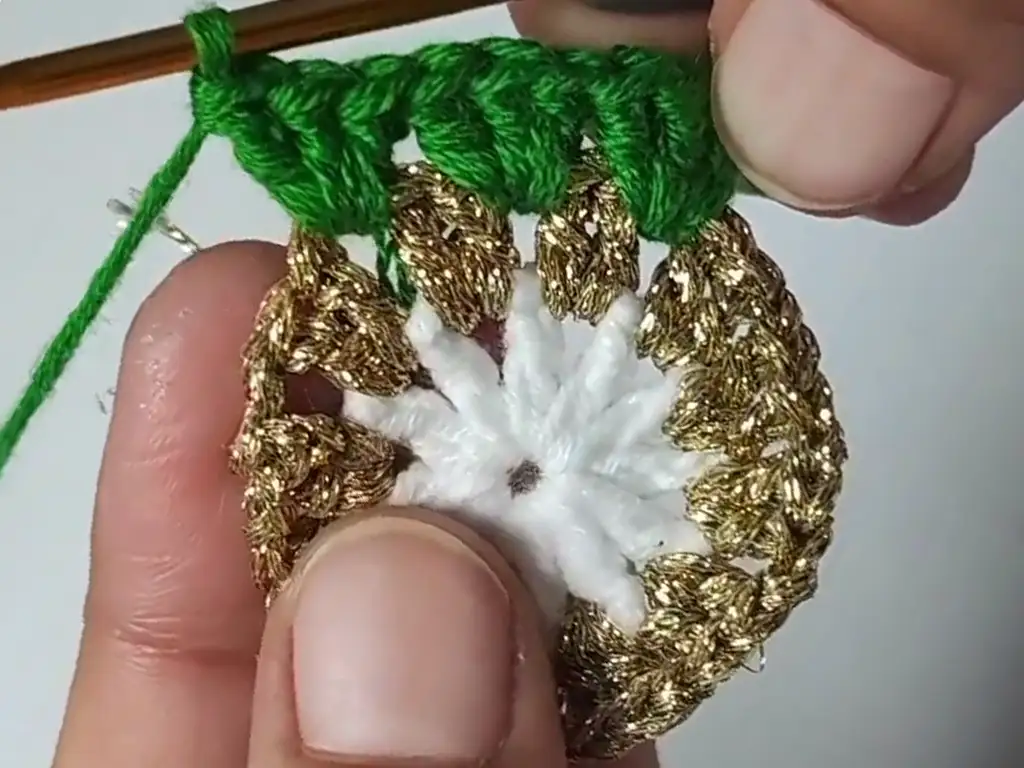 Hands crocheting the green row of the Christmas tree granny square, adding color and texture.