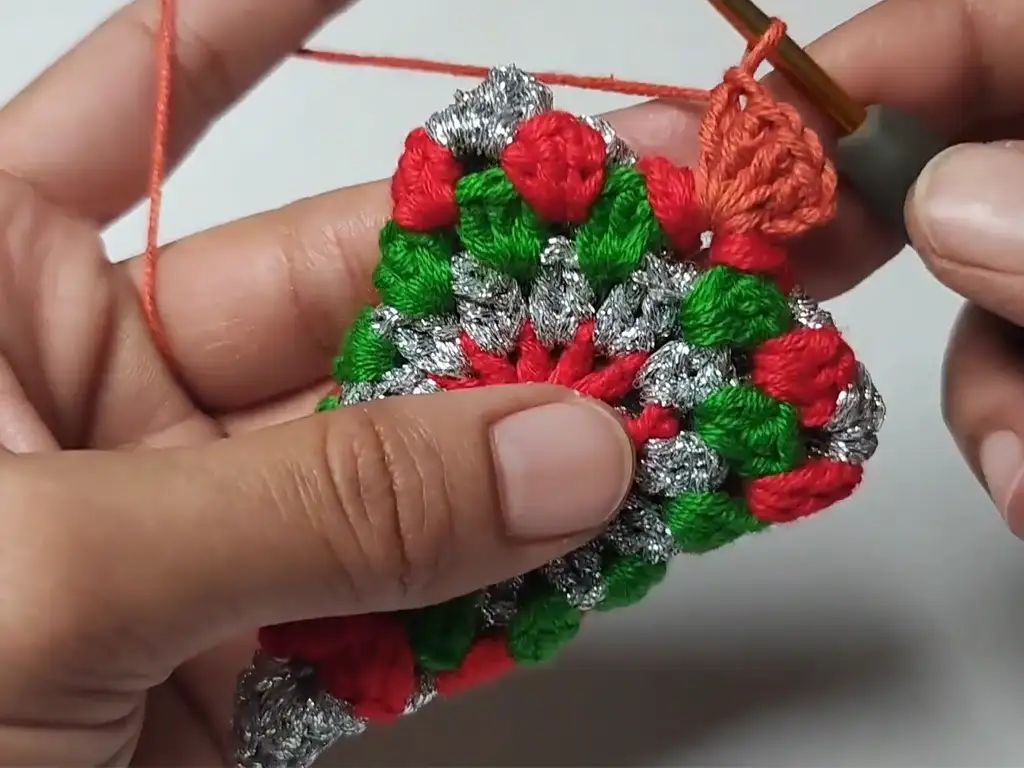 Close-up of hands crocheting the orange root section of the crochet Christmas tree ornament.