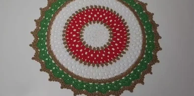A round crochet placemat in red, white, and green with gold accents.
