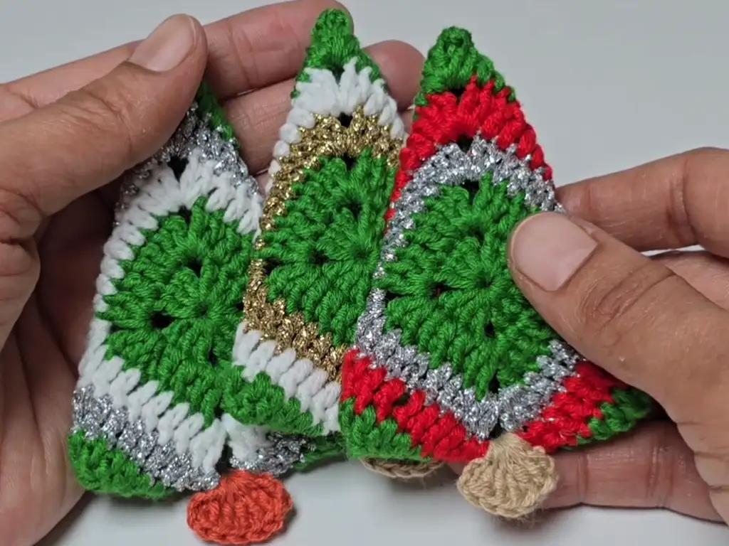 Three completed crochet Christmas tree ornaments in different color variations.