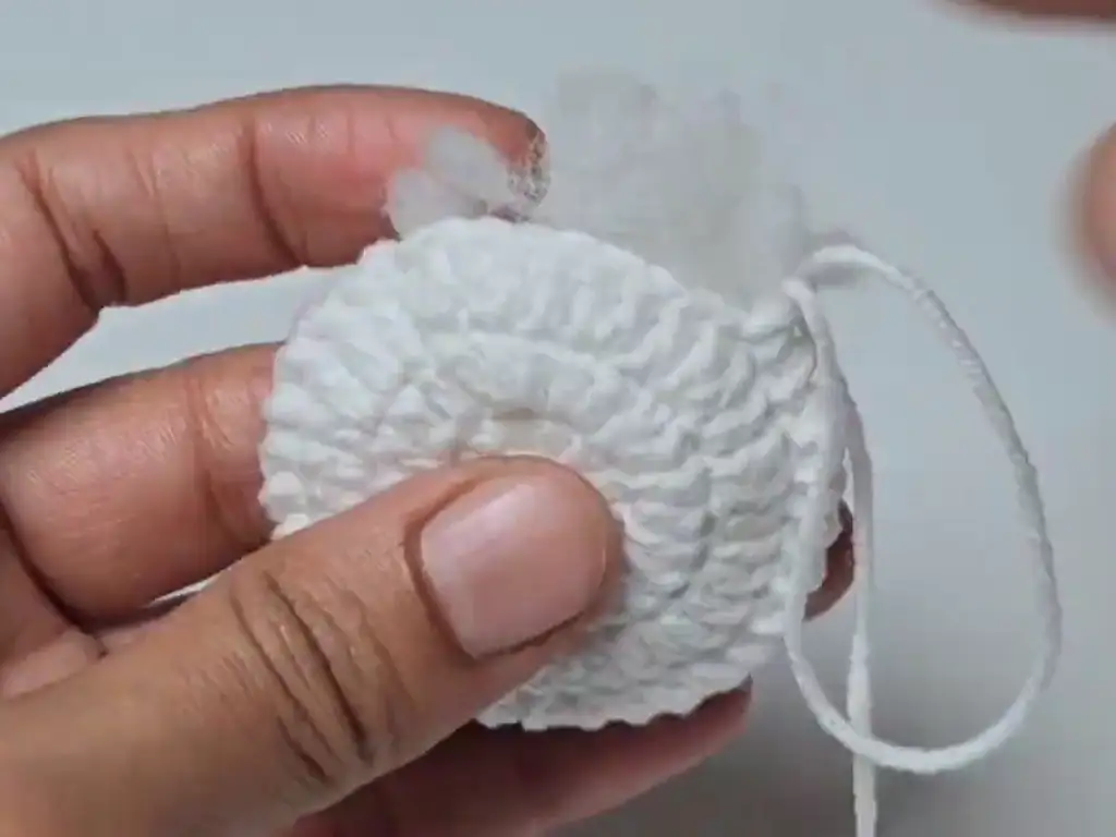 Adding fiberfill stuffing to a partially crocheted snowman head to give it shape and dimension.