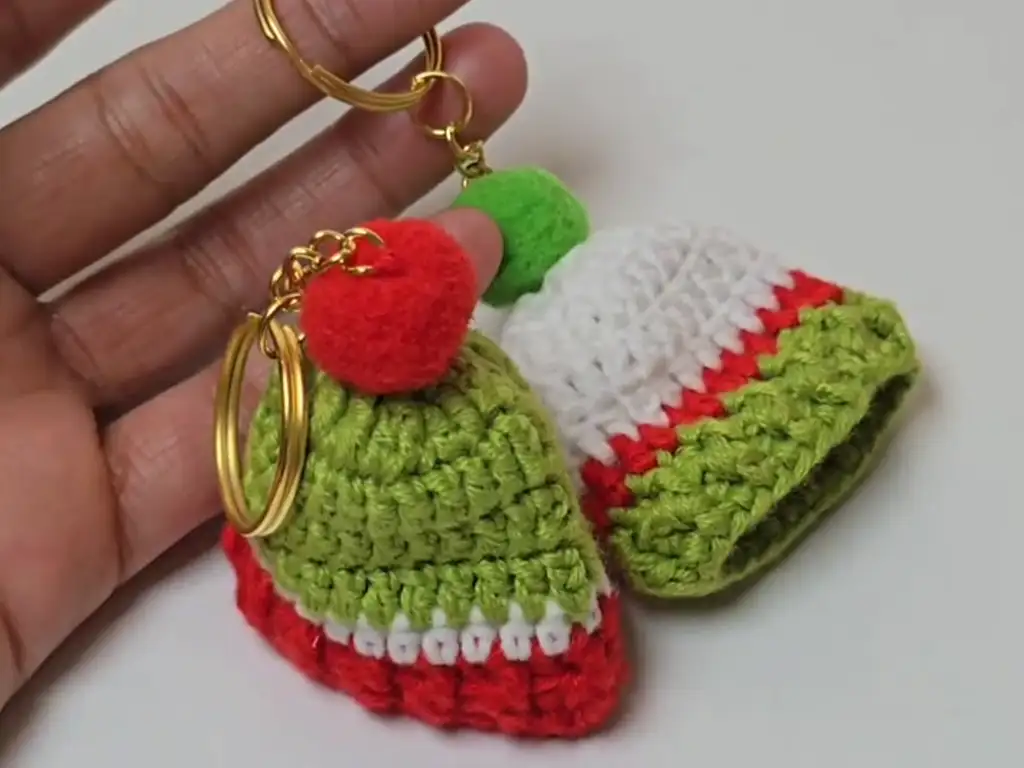 Two completed crochet Santa hat keychains, one held up to demonstrate size.