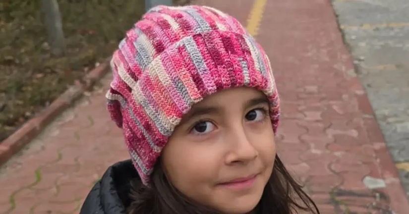 shows a child wearing the finished beanie, a striped beanie with pink and gray.