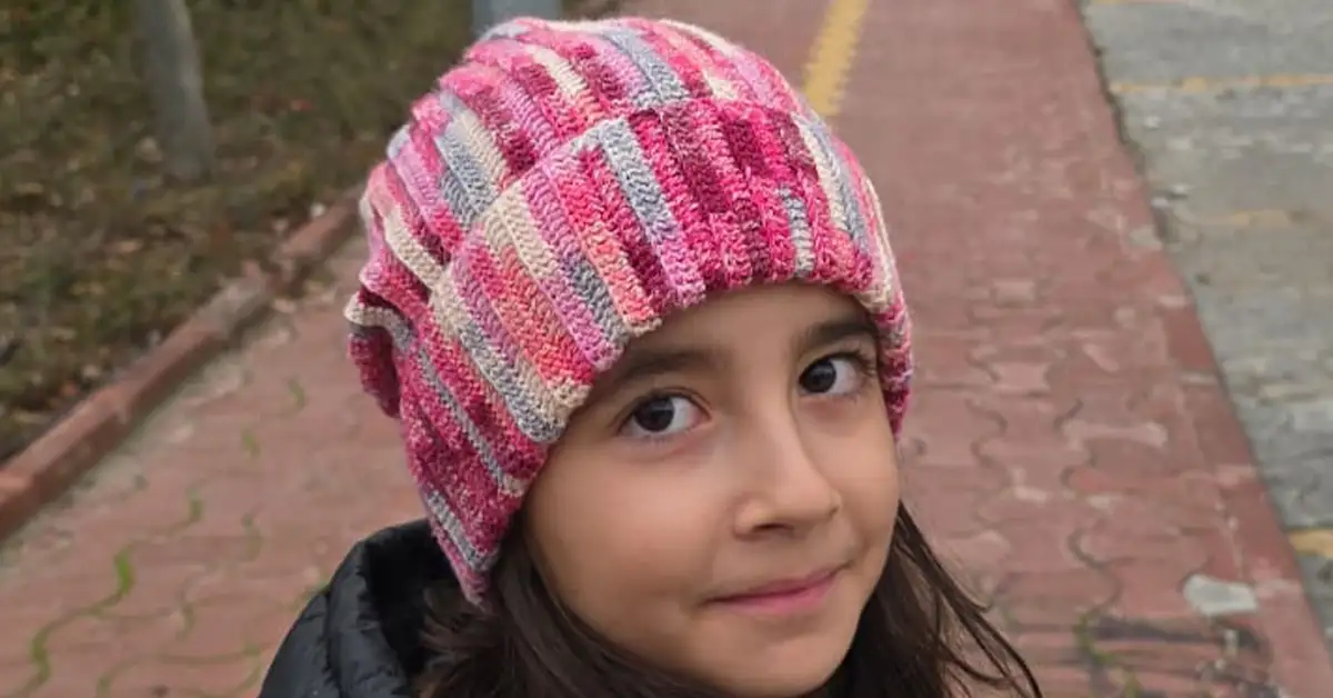 shows a child wearing the finished beanie, a striped beanie with pink and gray.