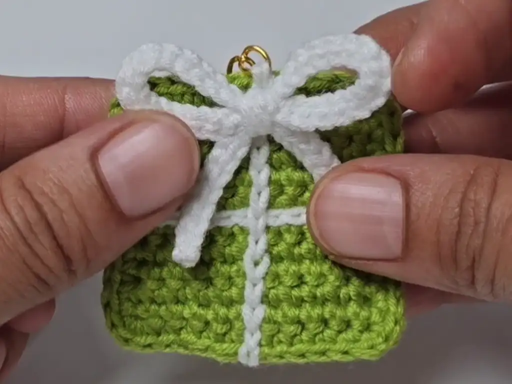 Completed green crochet gift wrap keychain with a white bow.
