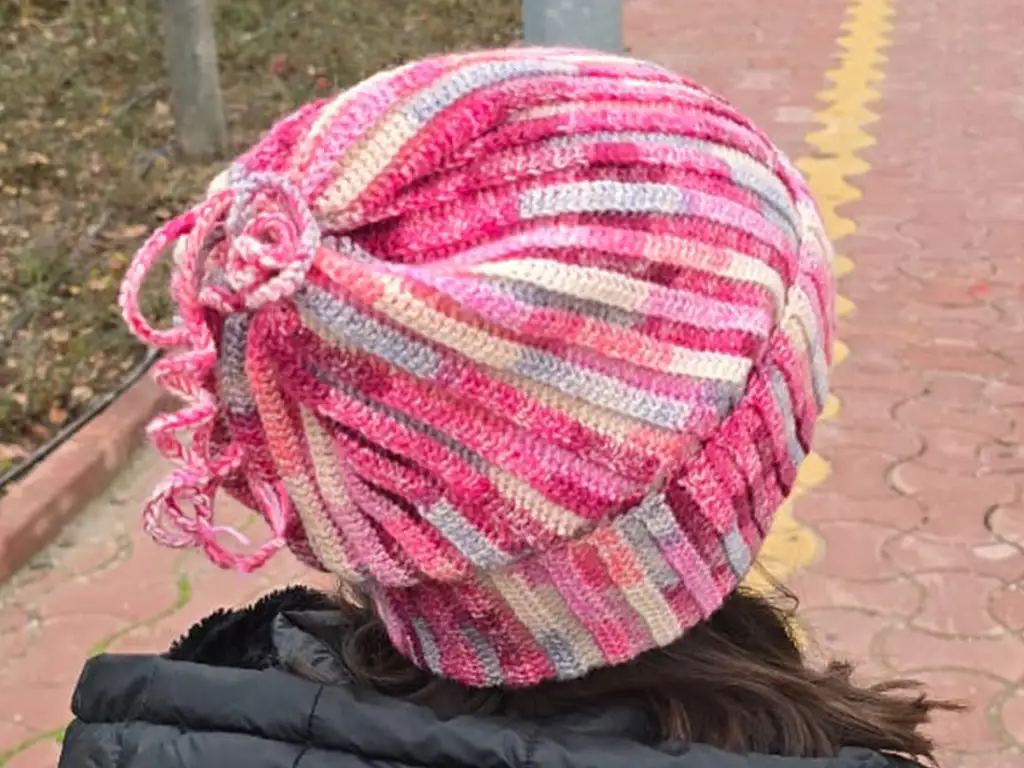 Child wearing pink and gray crochet beanie, side view, drawstring detail.