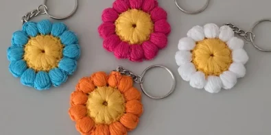 Four colorful crochet flower keychains in blue, pink, white, and orange, with yellow centers, displayed against a white background.