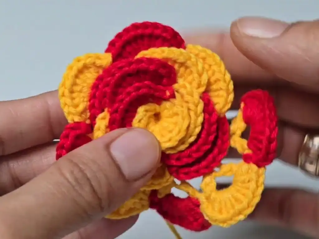 Partially completed crochet rose with red petals attached to a yellow base.