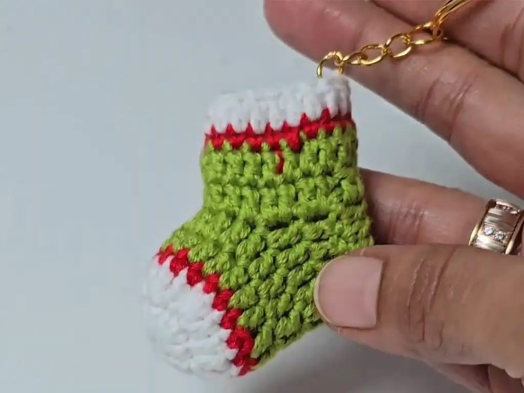 Completed mini Christmas stocking keychain, crocheted in green, red, and white.