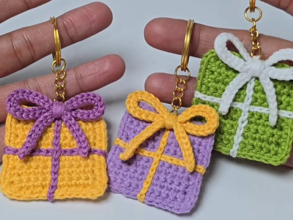 Three finished crochet gift wrap keychains in yellow, purple, and green.