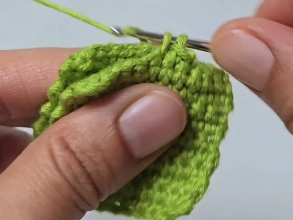 Hands using a crochet hook to join two green crochet squares.