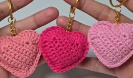 Three finished crochet heart keychains in varying shades of pink held up together.