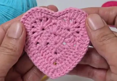 Completed pink crochet heart applique held between two hands, showcasing the stitch definition.