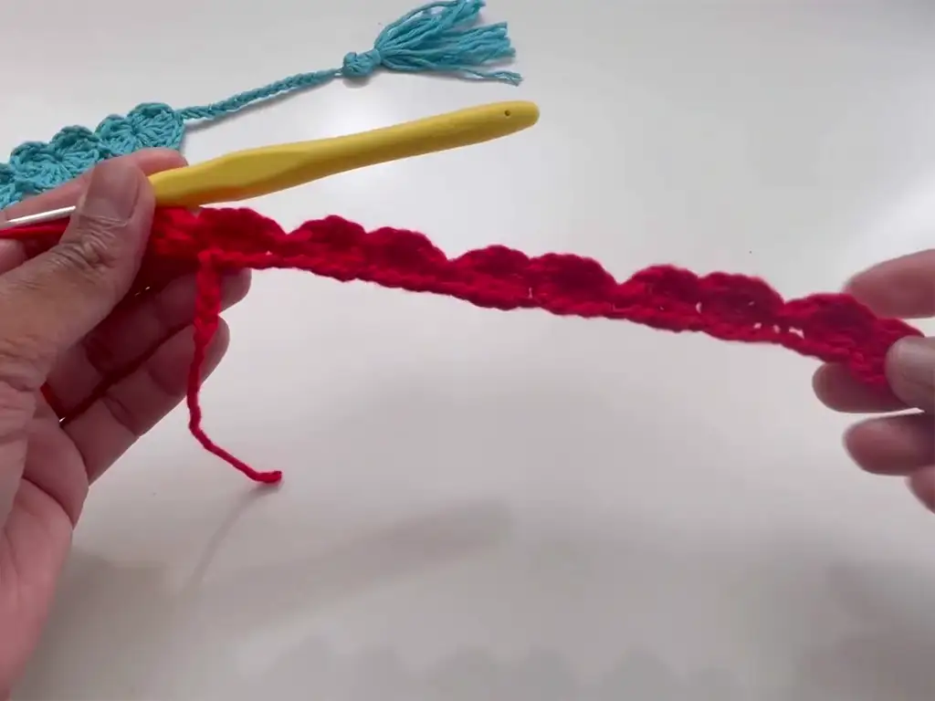 A partially crocheted red heart bookmark, showcasing the scalloped edge of the design.