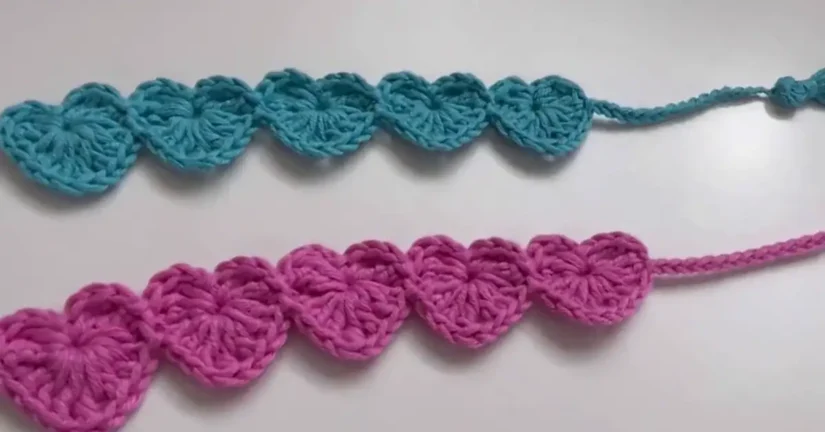 Two handmade crochet bookmarks with heart patterns in pink and blue, alongside a crochet hook.