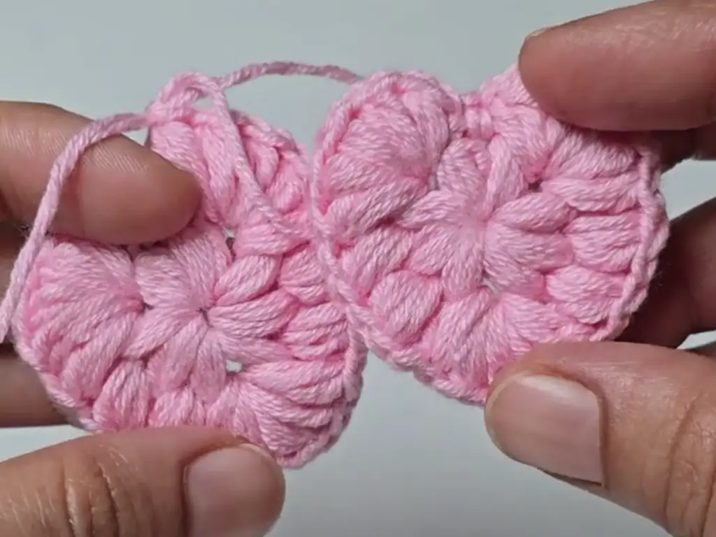 Two separate crochet heart keychain pieces are held side-by-side, illustrating the construction process before they are joined together.