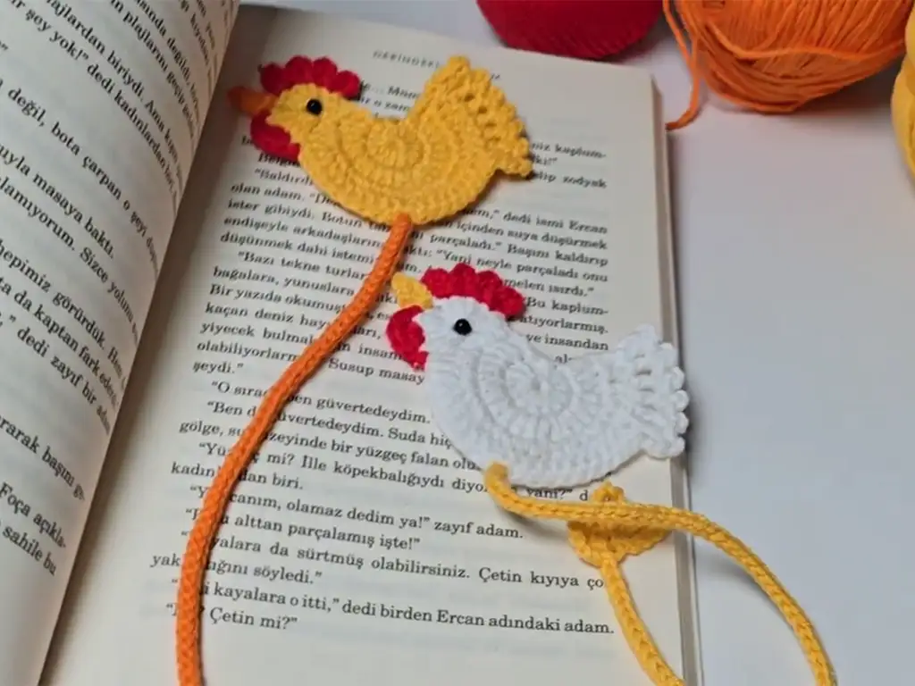 Two finished handmade crochet chicken bookmarks in action! These fun crochet gifts are shown marking pages in a book, demonstrating their practical use and adorable charm.