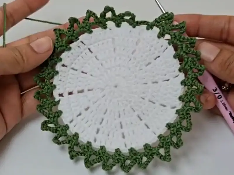 Green leafy border crocheted around the coaster base.