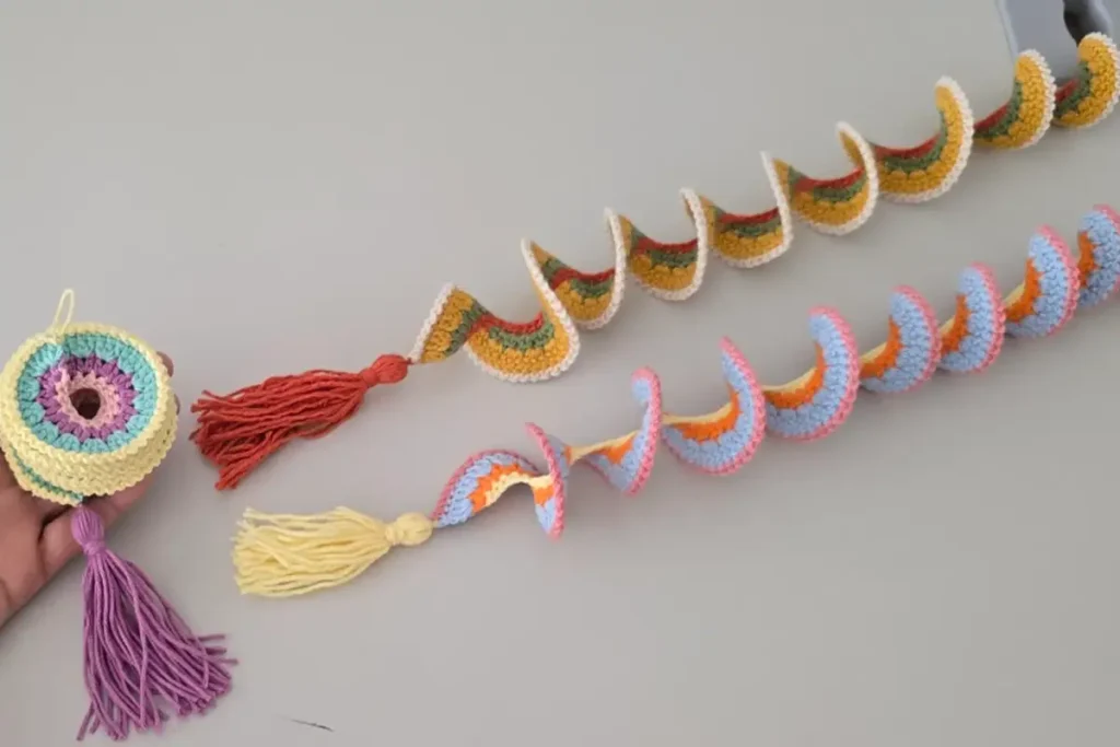 Hand holding a spiral crochet wind spinner with tassels — colorful yarn decoration laid out on a minimalist desk.