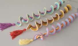 Three colorful crochet wind spinners with tassels, laid flat on a table – easy spiral crochet DIY decoration.