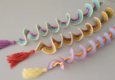 Three colorful crochet wind spinners with tassels, laid flat on a table – easy spiral crochet DIY decoration.