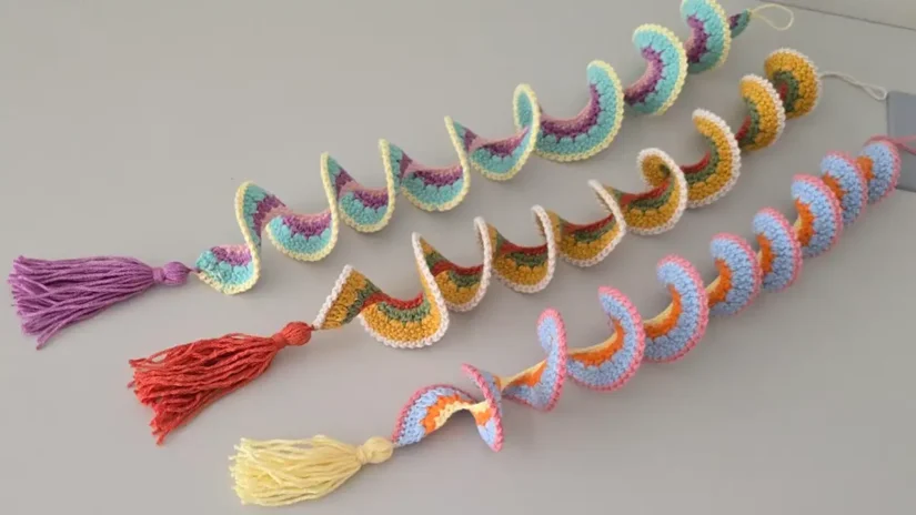 Three colorful crochet wind spinners with tassels, laid flat on a table – easy spiral crochet DIY decoration.
