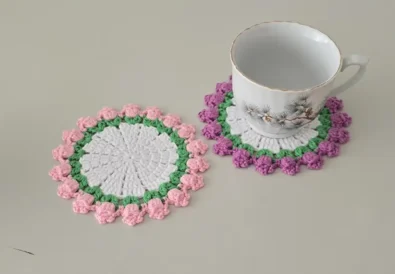 Hand holding a pink crochet tulip coaster with a purple one next to it