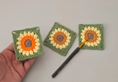 Crochet sunflower granny square held in hand – finished floral motif with green edging, made using puff stitch petals.
