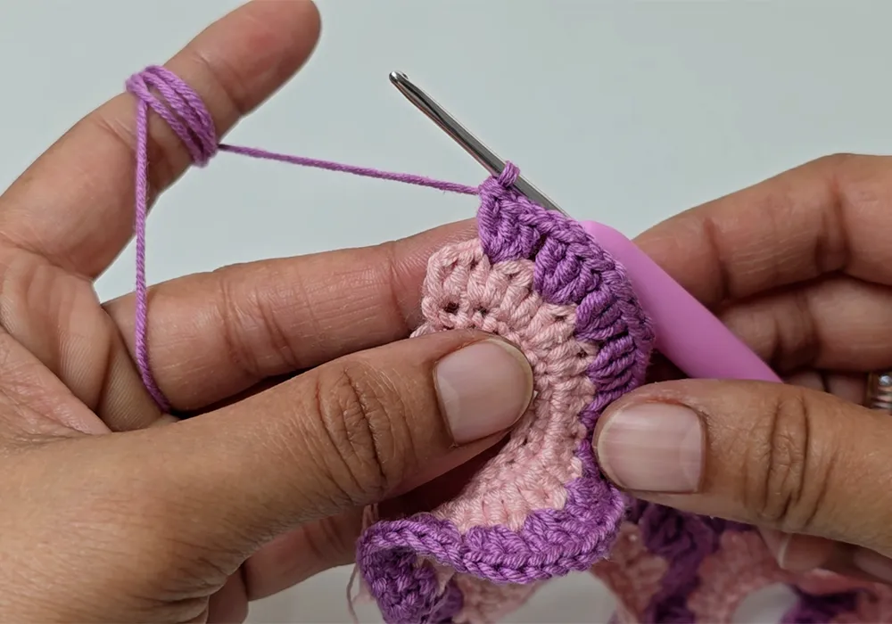 Crocheting the spiral shape using double crochet stitches with purple yarn.