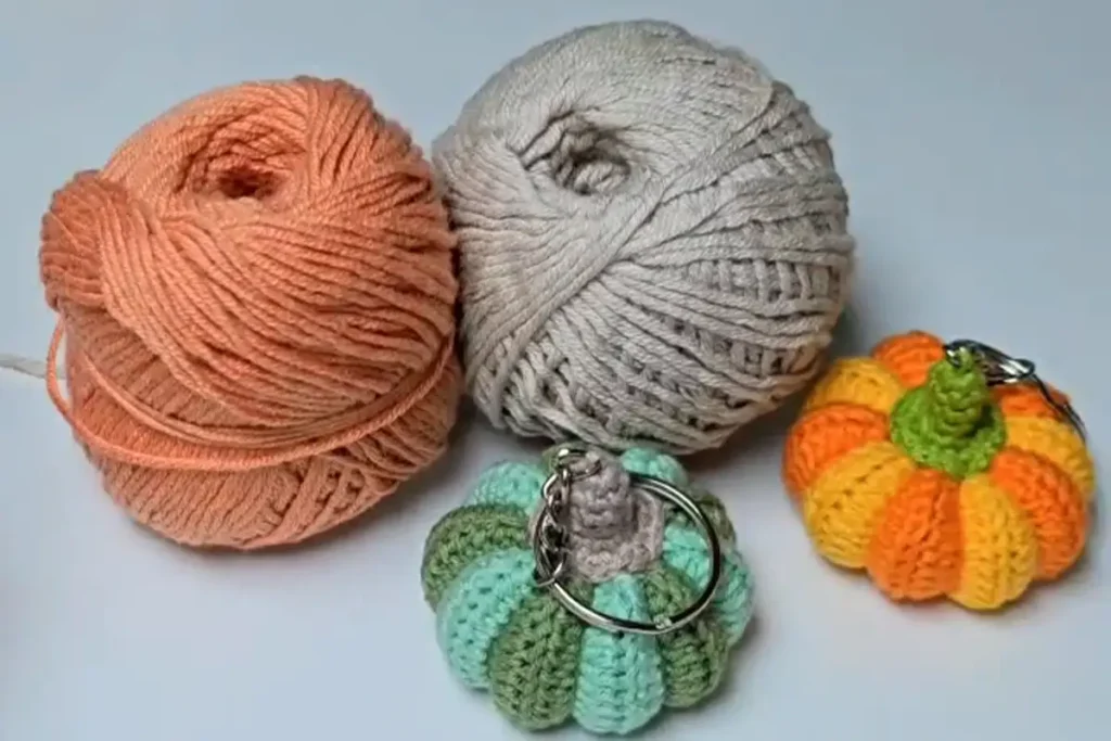 Yarn balls in orange, beige, and green with finished crochet pumpkin keychains beside them