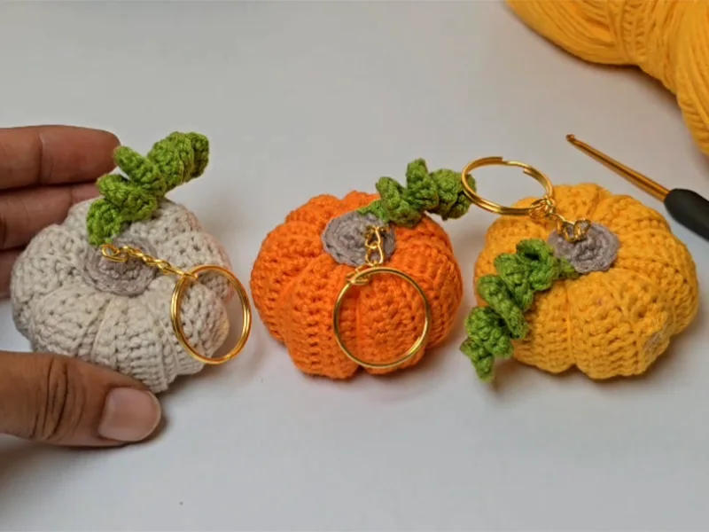 Three crochet pumpkin keychains in orange, white, and yellow colors