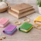 Colorful crochet book keychain set displayed on wooden table with mini handmade yarn book keychains in pink, purple, green and yellow