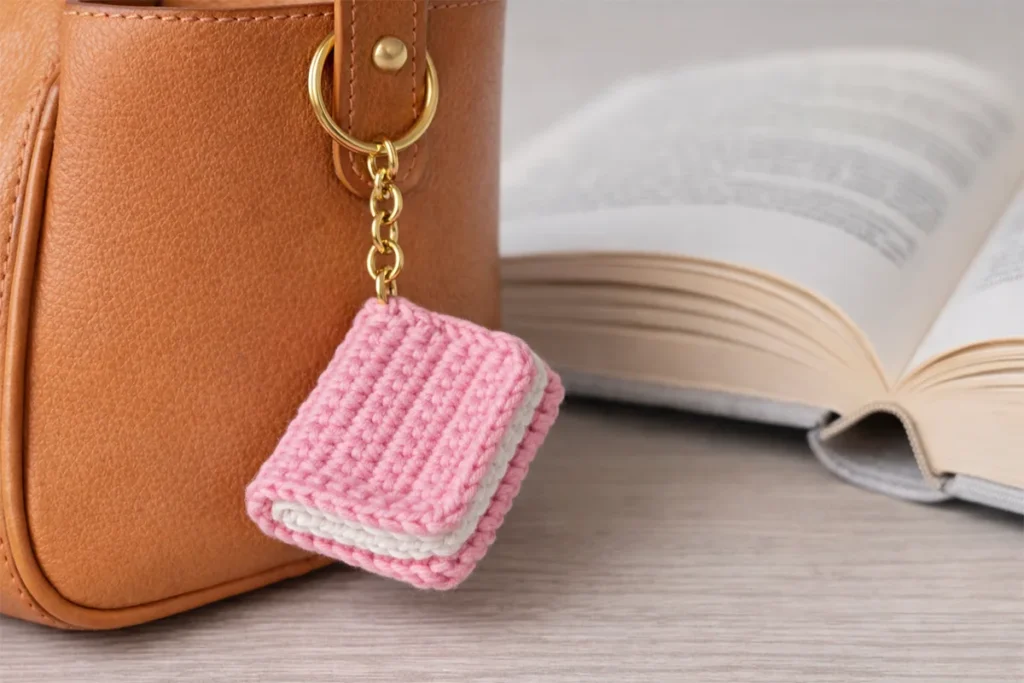 Handmade crochet book keychain attached to a bag, perfect small gift idea for book lovers.