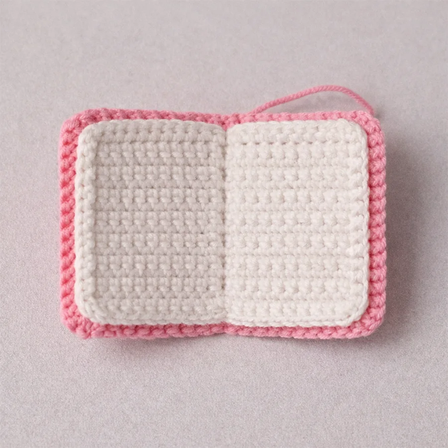 Close-up of white inner pages of a crochet book keychain with pink border, shown open flat.