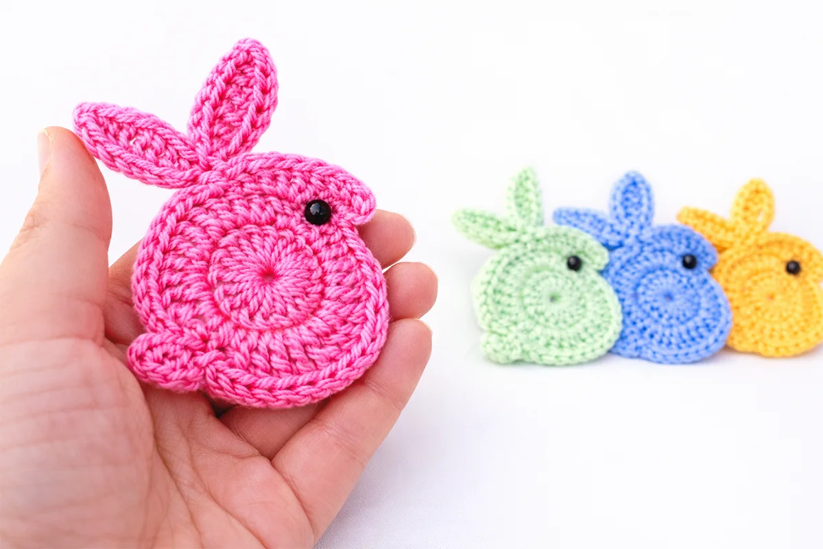 Easy crochet bunny applique for beginners held in hand with colorful crochet bunnies in background