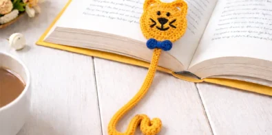 easy crochet cat bookmark pattern with curly tail and blue bow inside an open book, beginner friendly DIY crochet gift idea