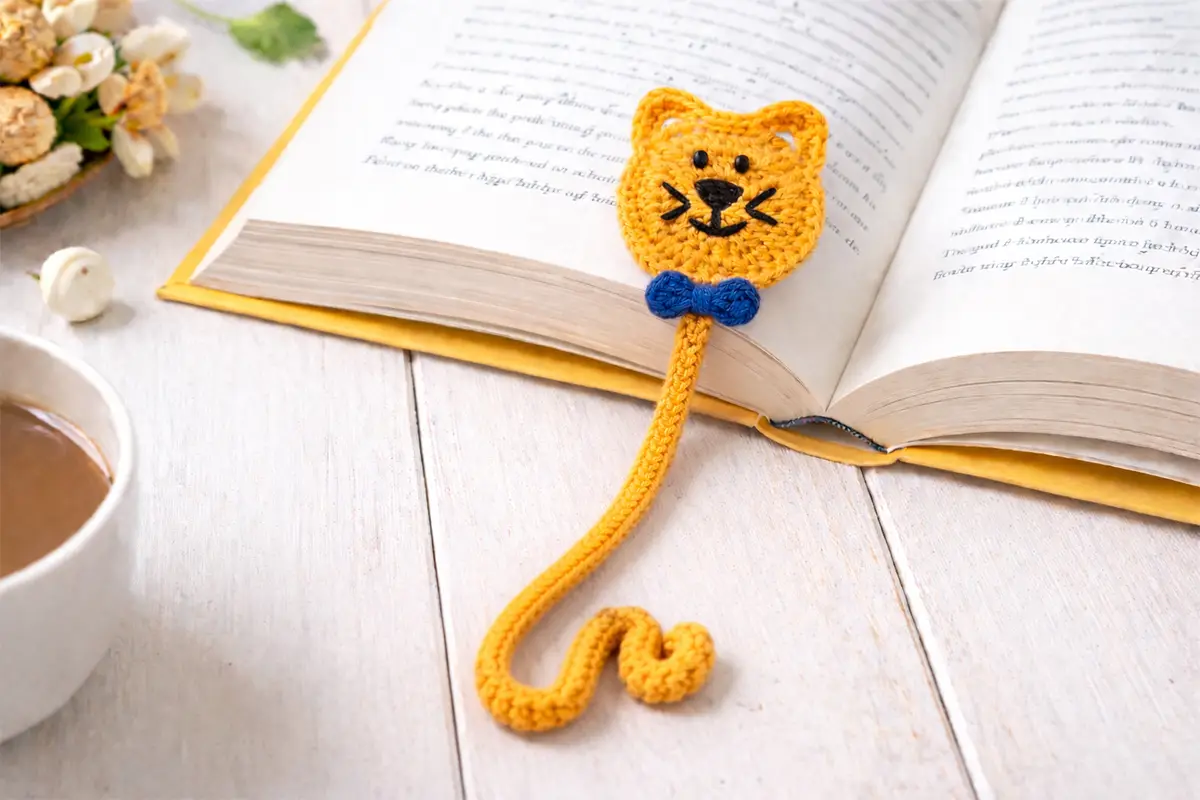 easy crochet cat bookmark pattern with curly tail and blue bow inside an open book, beginner friendly DIY crochet gift idea