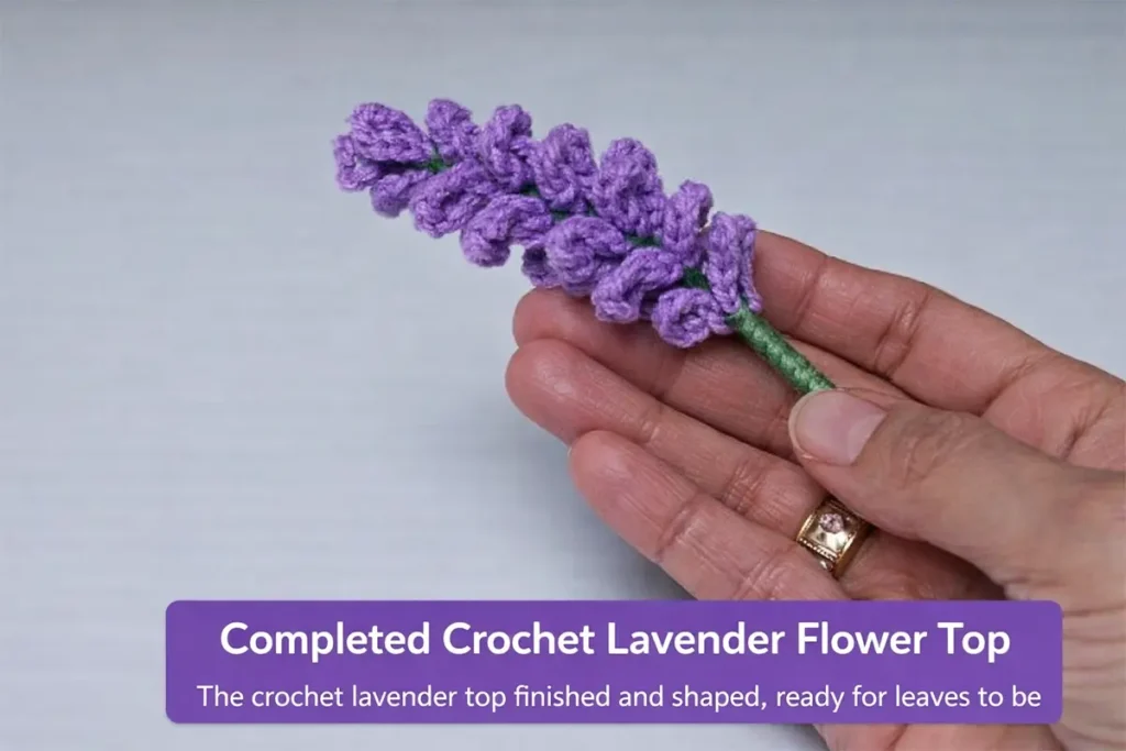 Finished crochet lavender stem with purple flower head and green leaves shown by hand on a clean background