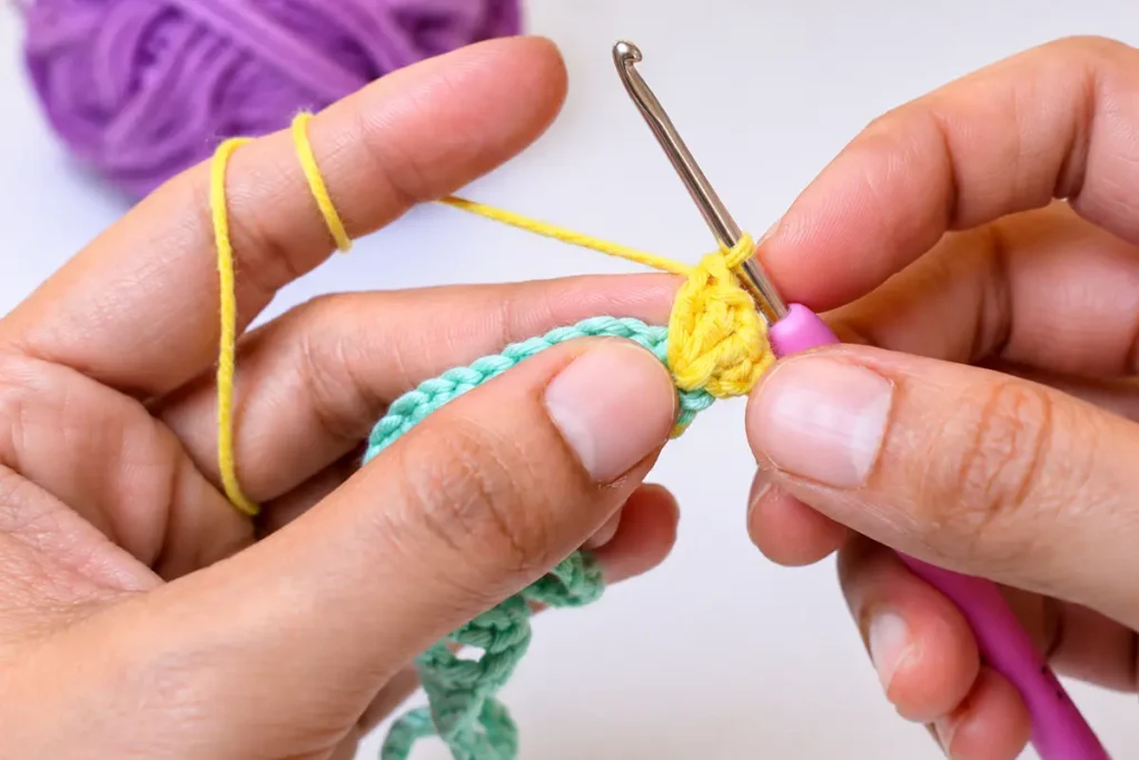 Hands adding the second color and making V-stitches in an easy crochet wind spinner pattern for beginners