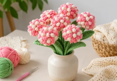 Realistic crochet flower bouquet in a small vase with cotton yarn balls and crochet hook on a clean craft table