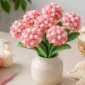 Realistic crochet flower bouquet in a small vase with cotton yarn balls and crochet hook on a clean craft table