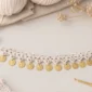 Crochet coin charm anklet made with white cotton yarn and gold coin charms on a soft neutral craft table with yarn and crochet hook