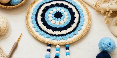 Crochet evil eye mandala with tassels, beads, and cotton yarn on a bright craft table