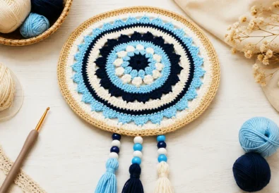 Crochet evil eye mandala with tassels, beads, and cotton yarn on a bright craft table