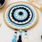 Crochet evil eye mandala with tassels, beads, and cotton yarn on a bright craft table