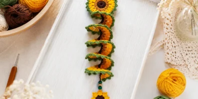 Crochet sunflower wind spinner pattern styled on a tray with yarn and crochet hook